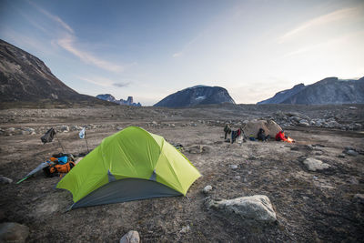 Two men prepare late dinner during dusk at arctic campsite.