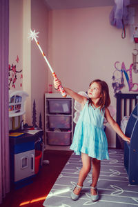 Cute girl wearing angel wings with magic wand standing at home