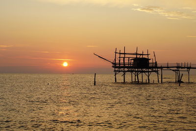 Silhouette pier over sea against sky during sunset