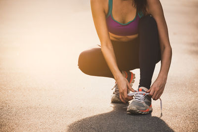 Low section of woman tying shoelace on road