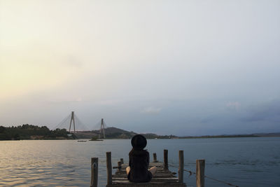 Rear view of woman sitting on pier over sea against sky