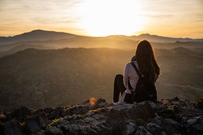 Rear view of woman sitting on rock at sunset