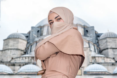 Portrait of young woman standing against buildings in city