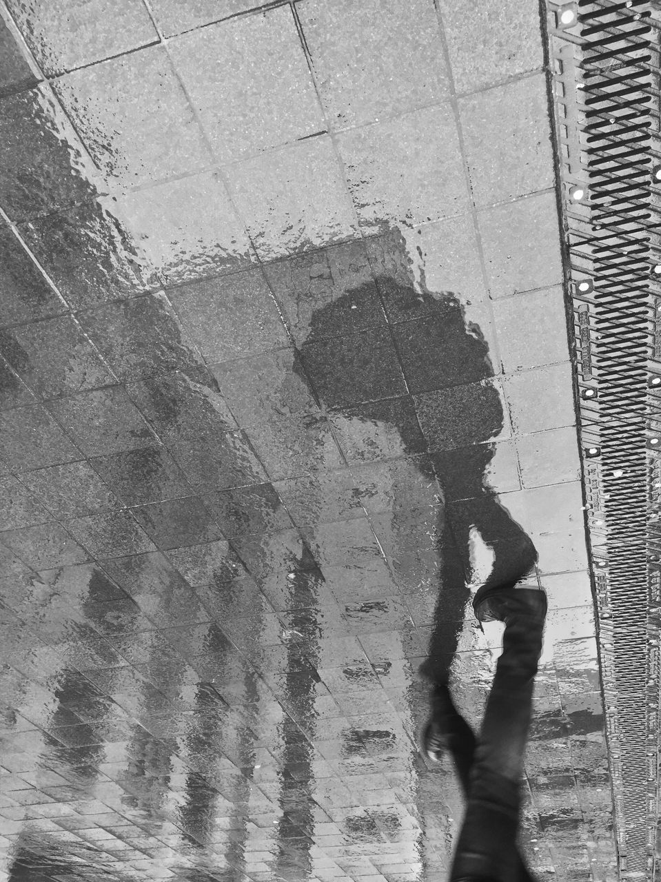 street, high angle view, shadow, wet, architecture, day, building exterior, built structure, sunlight, outdoors, road, lifestyles, puddle, textured, reflection, unrecognizable person, wall - building feature, sidewalk