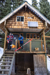 Full body young men with hockey gear smiling and looking at camera while standing on porch of wooden house in winter in british columbia, canada