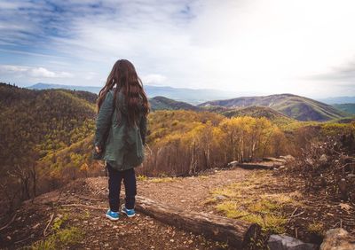 Rear view of woman standing in forest against sky