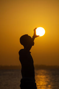 Silhouette woman standing against orange sky