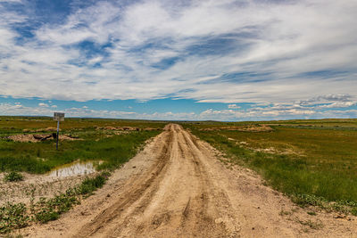 Dirt road amidst field against sky