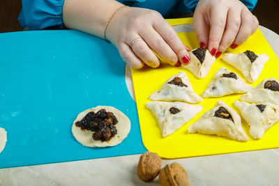 The hands of a jewish woman in a traditional headdress place triangular gomentashi cookies