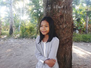 Portrait of smiling young woman standing by tree trunk