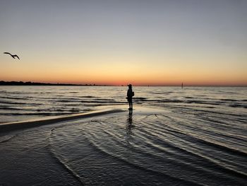 Silhouette man standing at beach against sky during sunset