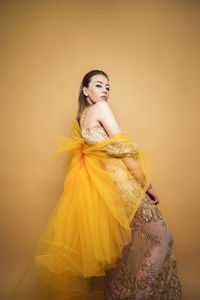 Portrait of young woman standing against yellow background