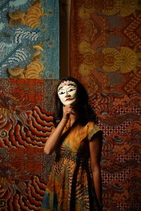 Portrait of smiling young woman holding mask against wall