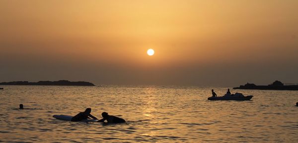 Silhouette people enjoying in sea against sky during sunset