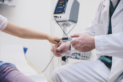 Midsection of mature doctor adjusting pulse oxymeter on girl's finger at hospital