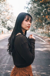 Portrait of young woman standing on road amidst trees in forest