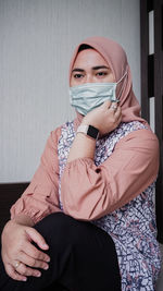 Portrait of a young woman sitting against wall