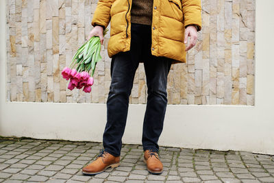 Blond man in a yellow winter jacket with a bouquet of tulips in hands