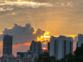 Buildings in city against dramatic sky during sunset