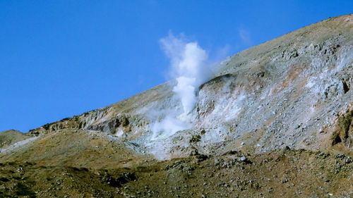 Low angle view of volcanic mountain against blue sky