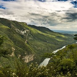 Scenic view of stream amidst green mountains against sky