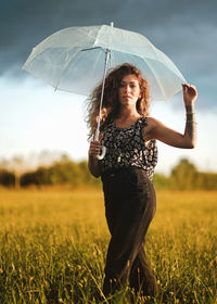 Full length of woman standing with umbrella on a field