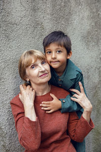 Child boy hugs his grandmother an elderly woman on the street against a gray wall