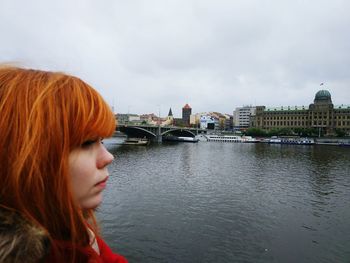 Woman looking at river in city against sky