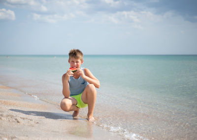 Side view of woman sitting at beach against sky