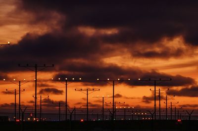 Silhouette street lights against dramatic sky during sunset