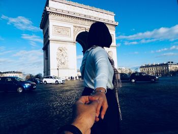 Cropped man holding woman hand on street near arc de triomphe