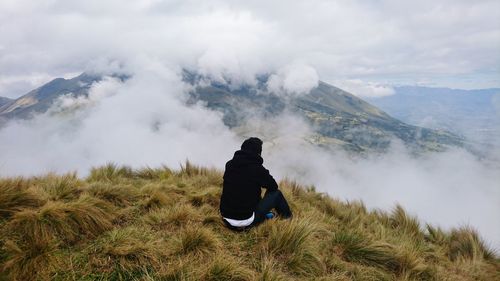 Rear view of man sitting on mountain against sky