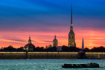 View of building by river against sky during sunset