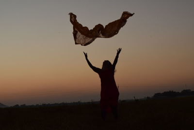 Silhouette woman standing on field against sky during sunset