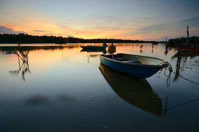 Boat moored in lake against sky during sunset