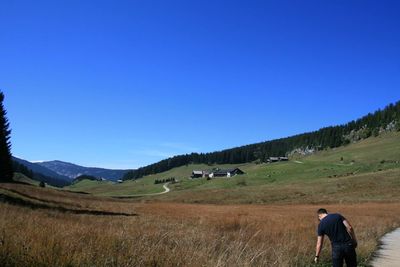 Rear view of man standing on field against clear blue sky