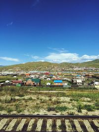 Houses on field by buildings against blue sky