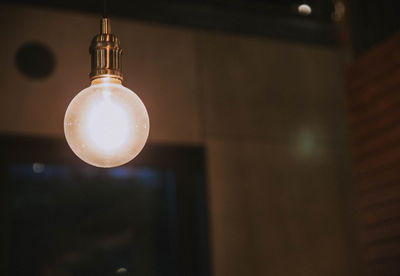 Low angle view of illuminated light bulb hanging from ceiling