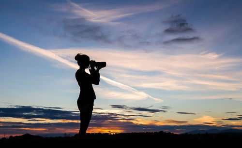 Silhouette woman photographing against sky during sunset