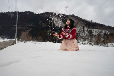 Smiling woman playing while kneeling on snow