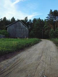 Dirt road amidst field against sky