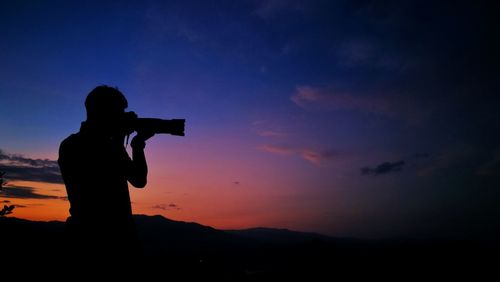 Silhouette man photographing against sky during sunset