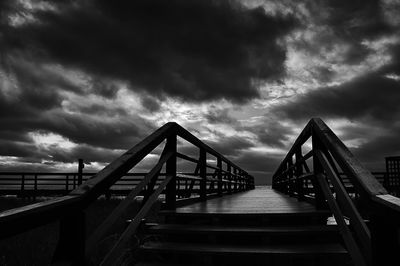 Bridge over calm sea against cloudy sky