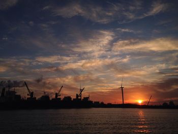 Silhouette cranes at harbor against sky during sunset