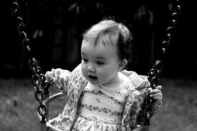 Cute baby girl sitting on swing in playground