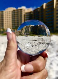 Close-up of hand holding crystal ball against sky