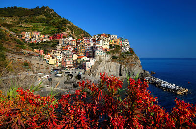 Residential district on rocky mountain by sea against clear blue sky