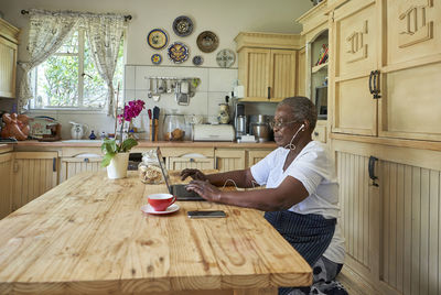 Senior woman sitting at kitchen table using laptop