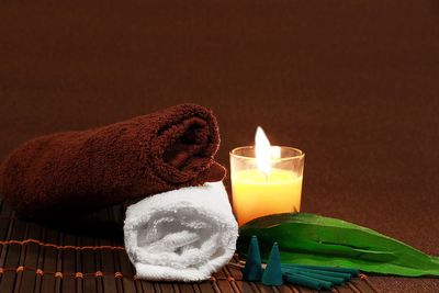 Close-up of burning candle with towels and leaf on table