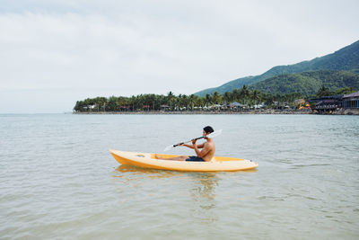 Man kayaking in sea against sky